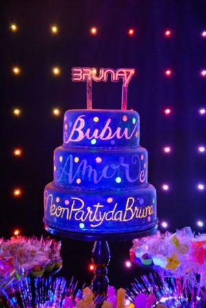 A Quinceanera birthday cake, featuring a three tiered design and a neon sign on top