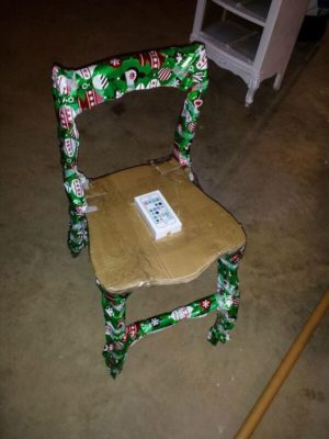 An iPhone wrapped in gift wrapping paper with a sticker on it, and a chair made out of wrapping paper imitating a Quinceanera theme.