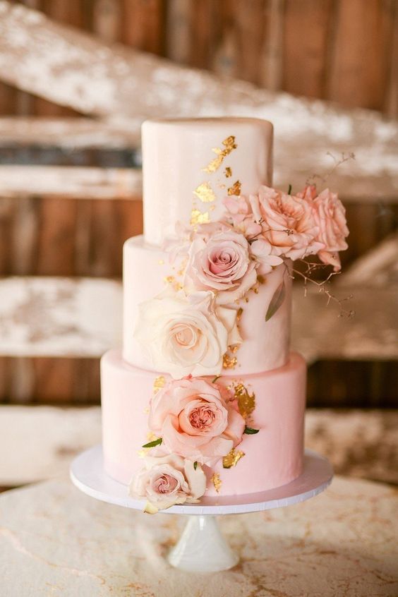 A three layer Quinceanera cake with pink and gold icing, adorned with flowers on top