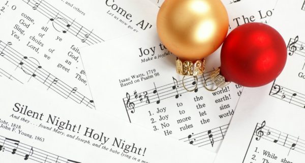 A red and gold Christmas ornament sitting on top of sheet music, representing a Quinceanera celebration with Christmas carol vibes