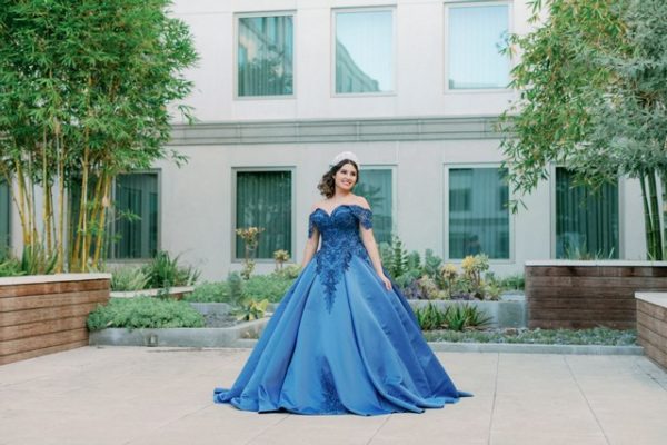 Quinceanera gown, a woman in a blue dress standing in front of a building