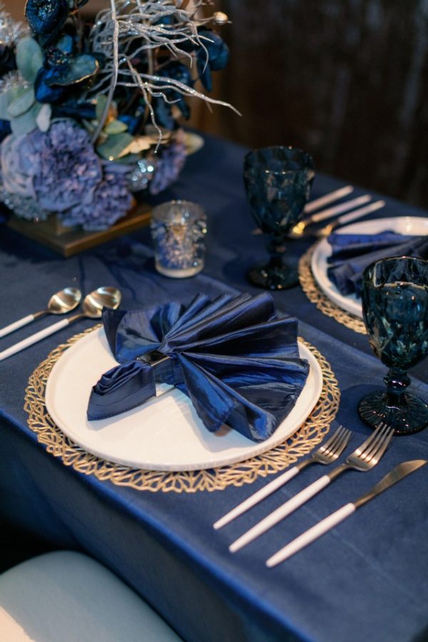 A Quinceanera themed cobalt blue table set with a blue table cloth and place settings