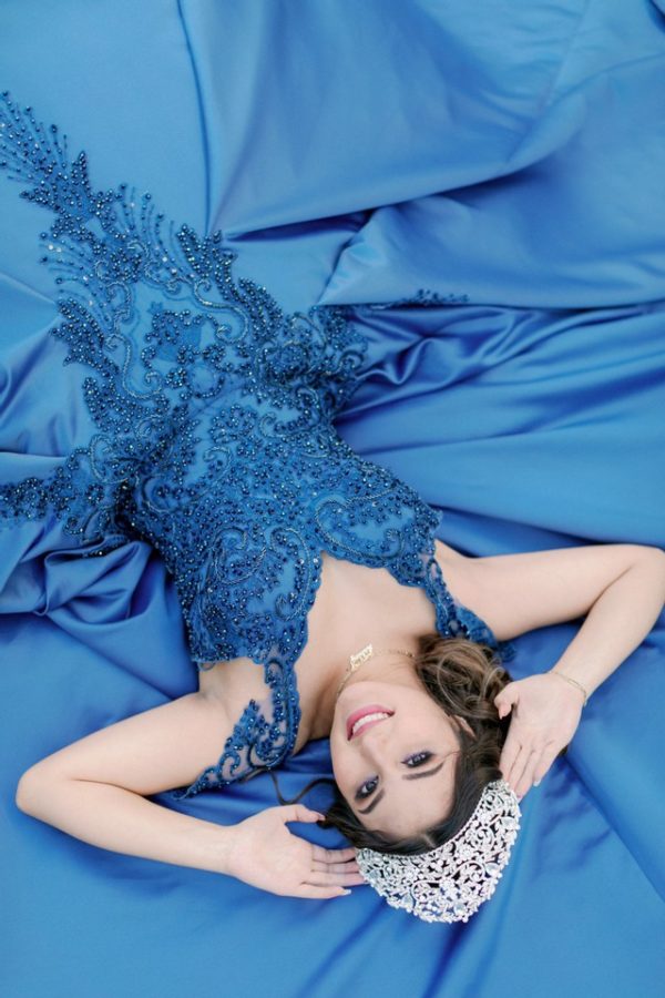 Beauty Quinceañera, a woman in a blue dress laying on a blue sheet