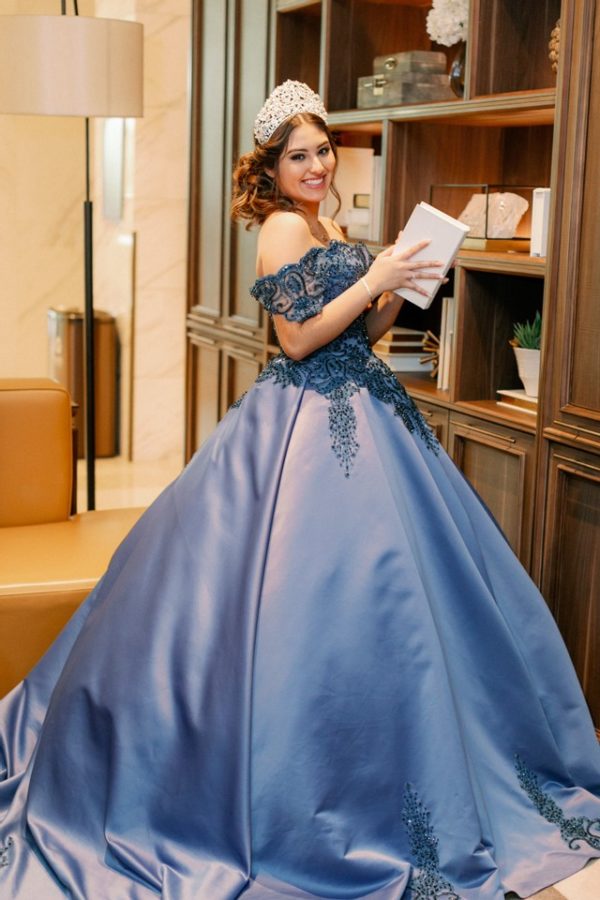 A woman in a blue ball gown reading a book at a Quinceanera event.