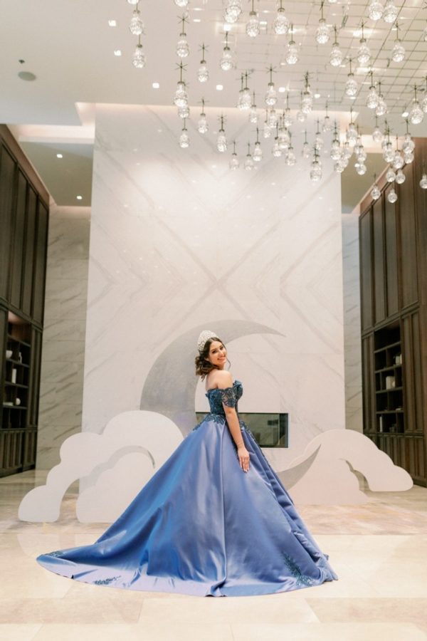 A Quinceanera gown: a woman in a blue dress standing in front of a chandelier