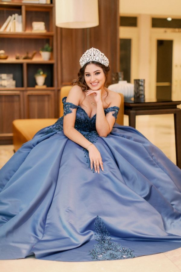 A woman wearing a blue Quinceanera gown sits on the floor, with a tiable