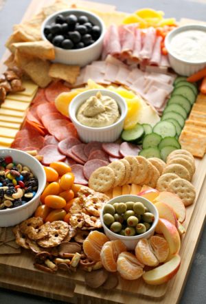 Quinceanera food board: A wooden cutting board topped with a variety of foods, including a charcuterie board