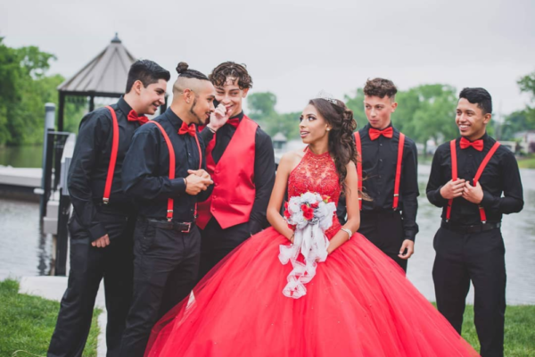 A group of people standing next to each other wearing rojo chambelanes de 15 años Quinceañera dresses.