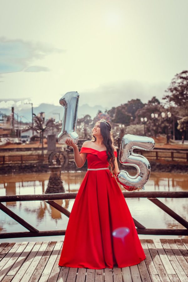 A photo shoot of a woman in a red dress holding a number five balloon for a Quinceanera celebration