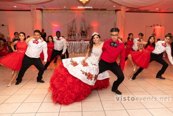 A group of people dressed in red and white dancing at a red themed Quinceañera party