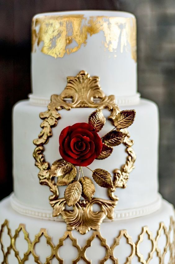 A pastel Quinceanera cake inspired by the beauty and the beast theme, featuring white and gold details and a red rose on top.