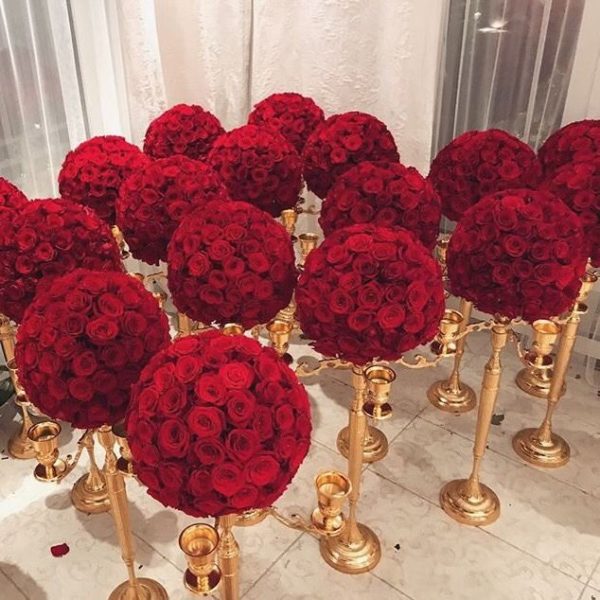 A beautiful Quinceanera decoration with red and gold accents, including Quinceañera dresses and a bunch of red roses in gold vases.