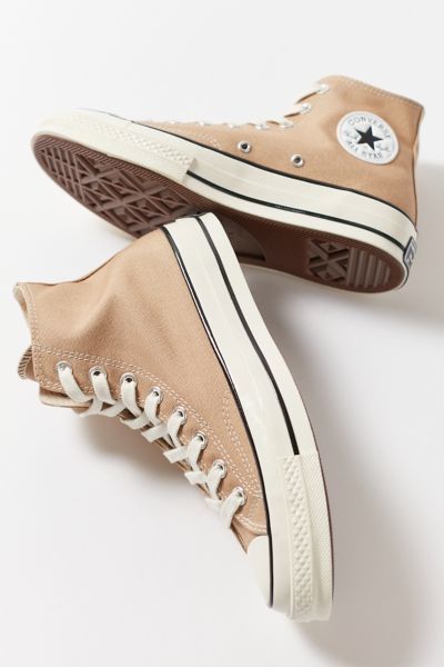 A pair of tan converses for a Quinceanera positioned on a white surface outdoors.