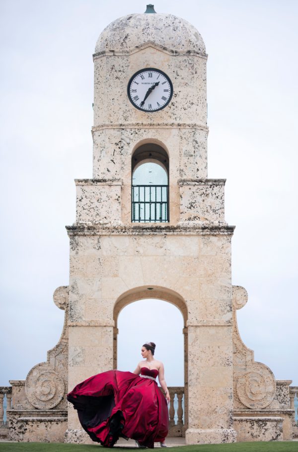 Selena, a woman in a red dress standing in front of a clock tower at a Quinceanera