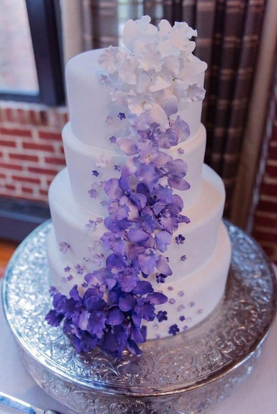 A Quinceanera cake with a purple ombre design, adorned with purple and white flowers