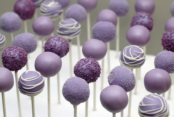 A bunch of light purple cake pops sitting on top of a white cake