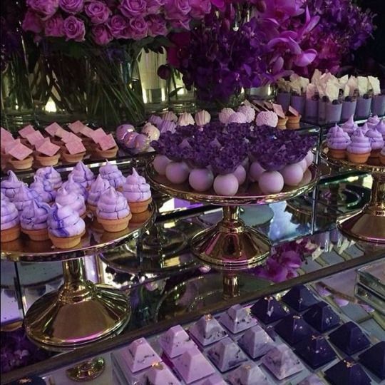 A display case filled with lots of different types of lilac cupcakes for a Quinceanera celebration.