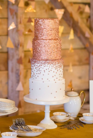 A three-tiered Quinceanera cake in rose gold, displayed on a table.