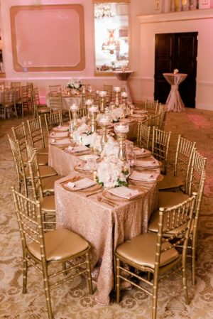 A table set for a Quinceanera reception with rose gold decorations and gold chairs