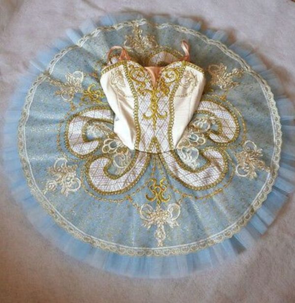 A beautiful Quinceanera dress with blue and white embroidery, resting on a bed.