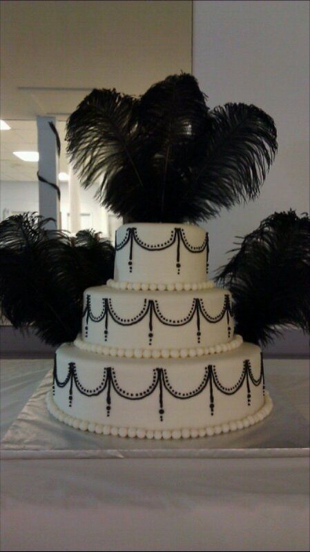 A Quinceanera cake with an old Hollywood theme. It is a three-tiered cake with black feathers on top.