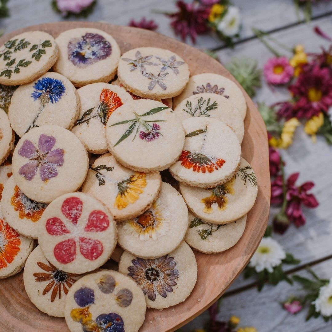 A wooden plate filled with Quinceanera themed cookies, decorated with flowers and presented in a cottage core style.