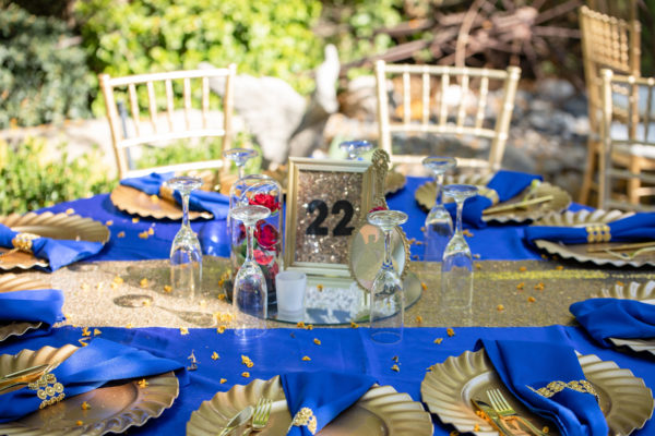A Quinceanera table set with a Majorelle Blue table cloth and gold place settings.