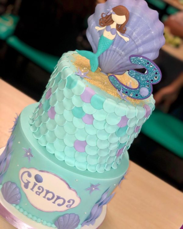 A Quinceanera cake decorated with sugar and featuring a little mermaid on top