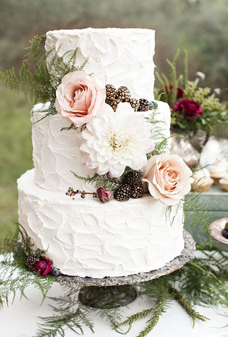 Quinceanera cake with textured buttercream icing, adorned with flowers and greenery, placed on a table
