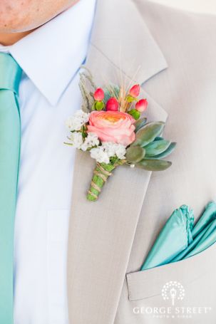 Close up of a person wearing a mint and coral Quinceanera suit and tie, with a Quinceanera invitation