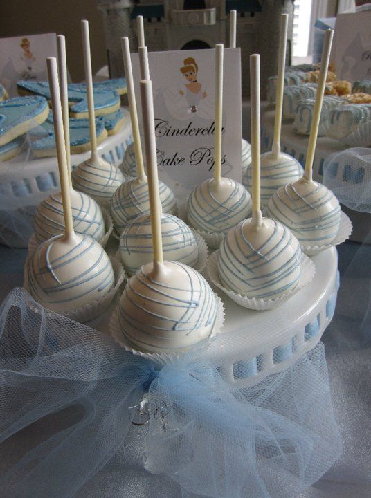 A Quinceanera themed image featuring a buttercream cake, as well as a table topped with cake pops covered in white and blue frosting.