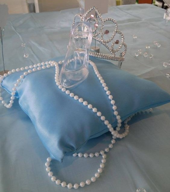 A Quinceanera themed image featuring cinderella centerpieces table with a blue pillow adorned with pearls and a tiable on it.