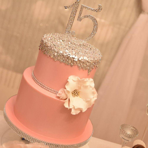 A salmon-colored Quinceanera cake with a white flower on top
