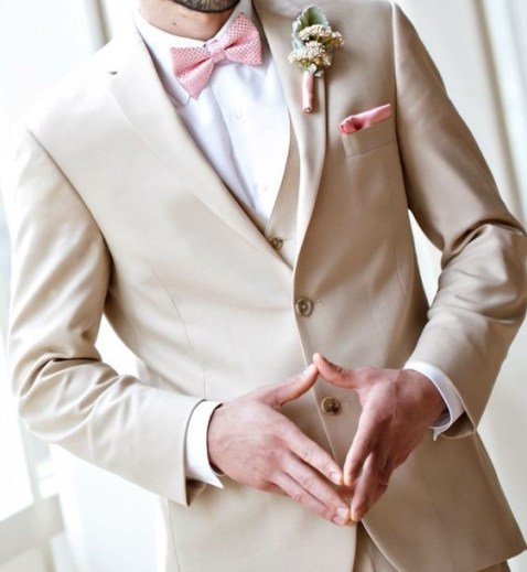 A man in a rose gold chambelanes suit, wearing a tan suit and a pink bow tie