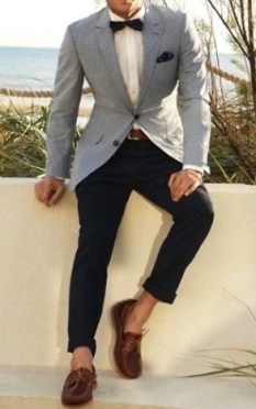 A man in a suit and bow tie sitting on a wall, wearing a Greek Quinceanera outfit for men