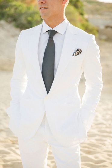 A man in a white suit and tie standing on a beach at a Quinceanera event