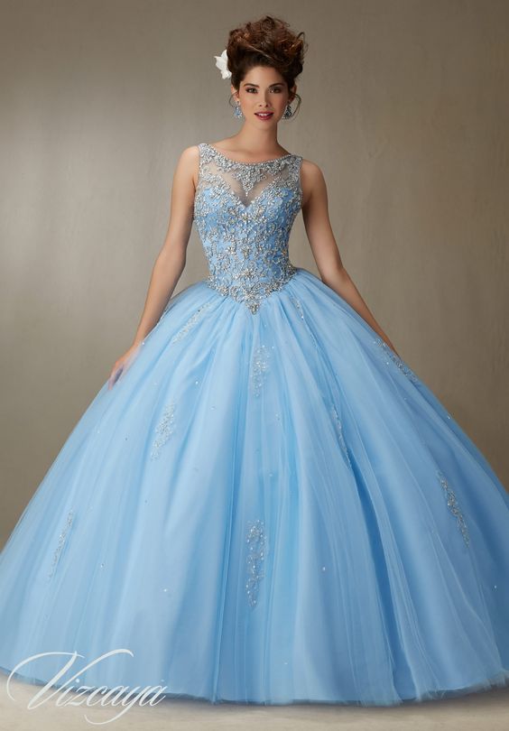 A woman in a blue ball gown posing for a picture at a Quinceanera event, wearing a Morilee dress by Mori Lee