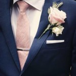 A close up of a person wearing a navy suit with a dusty rose tie, suitable for a Quinceanera celebration.