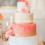 A Quinceanera inspired three-tiered cake with coral and gold colors, adorned with pink flowers on top