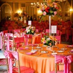 A Quinceanera reception in a spacious function hall with pink and orange floral design. The banquet room is adorned with tables and chairs in matching colors.