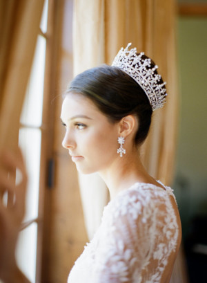 A woman wearing a tiara and a round crown hairstyle, looking out a window