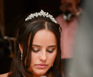 A woman in a Quinceanera dress wearing a crown tiara and holding a microphone