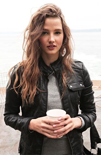 A beautiful woman in a leather jacket holding a cup of coffee at a Quinceanera event.