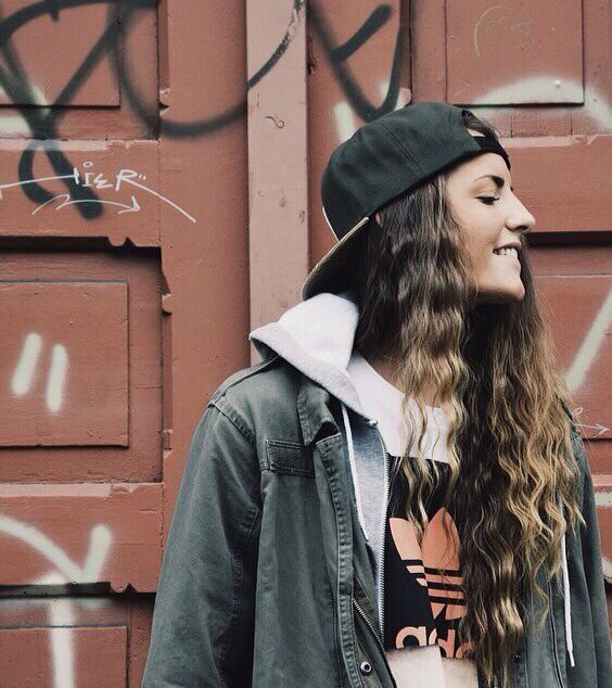 A woman with long hair wearing a hat and jacket while wearing a Quinceanera-themed beanie T-shirt.