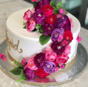 A beautiful Quinceanera cake with white frosting decorated with pink and purple flowers on top