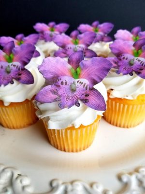 A Quinceanera themed cupcake on a white plate, showcasing cupcakes covered in purple flowers.