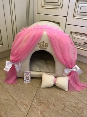 A white dog sitting on a Quinceanera-themed dog house decorated with pink and white bows