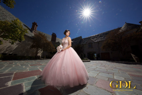 Quinceanera photograph of a woman in a pink dress standing in a courtyard wearing a Quinceanera Dress