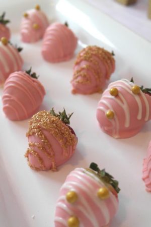 Quinceanera party image with pink gold strawberries. The image shows a white plate topped with pink chocolate covered strawberries.