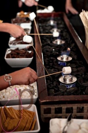 A group of people standing around a table filled with food bar a smores S'more at a Quinceanera celebration
